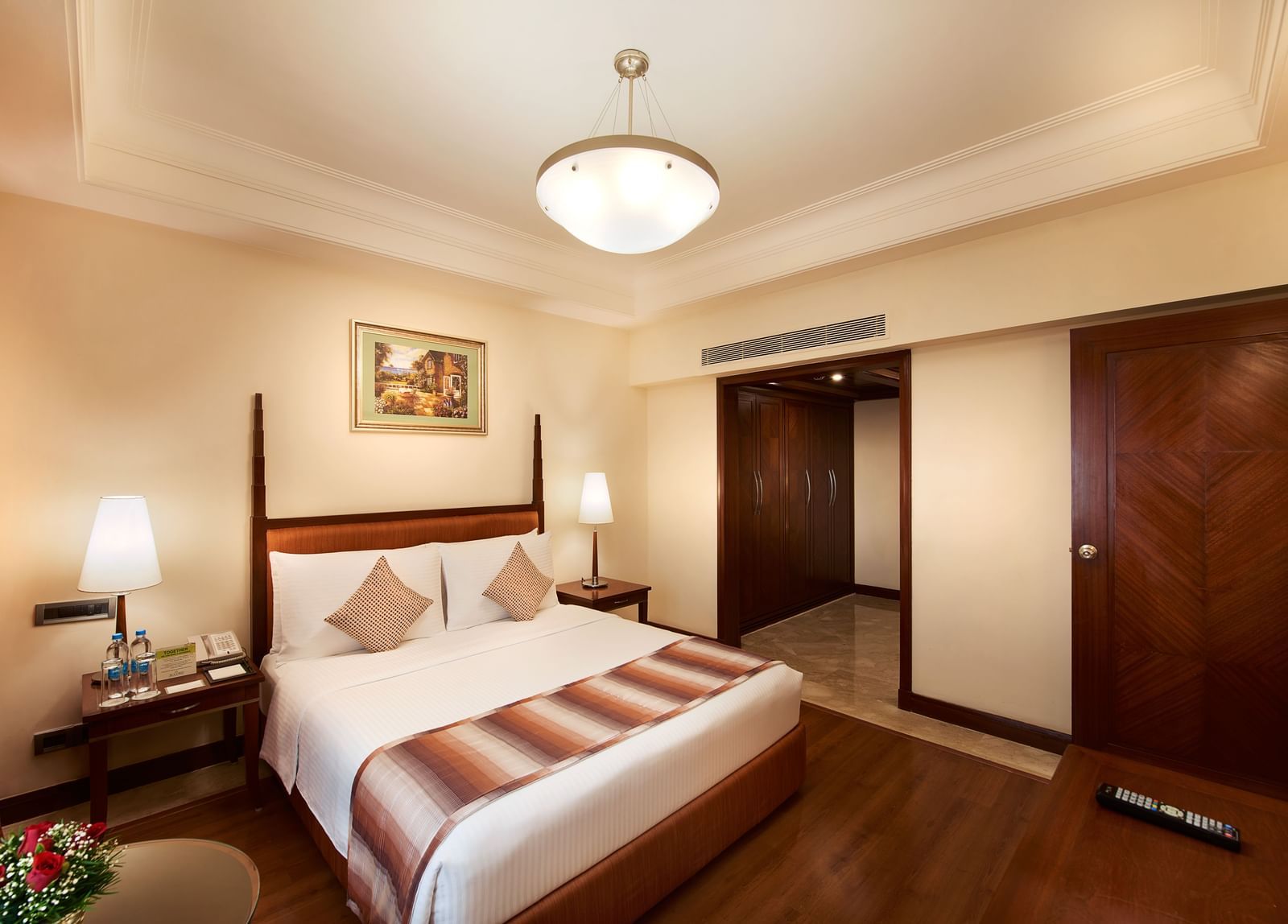 An image of a bedroom with a double size bed, bedside lamp on either side, a table with vase, and a wardrobe - Accord Hotels and Resorts